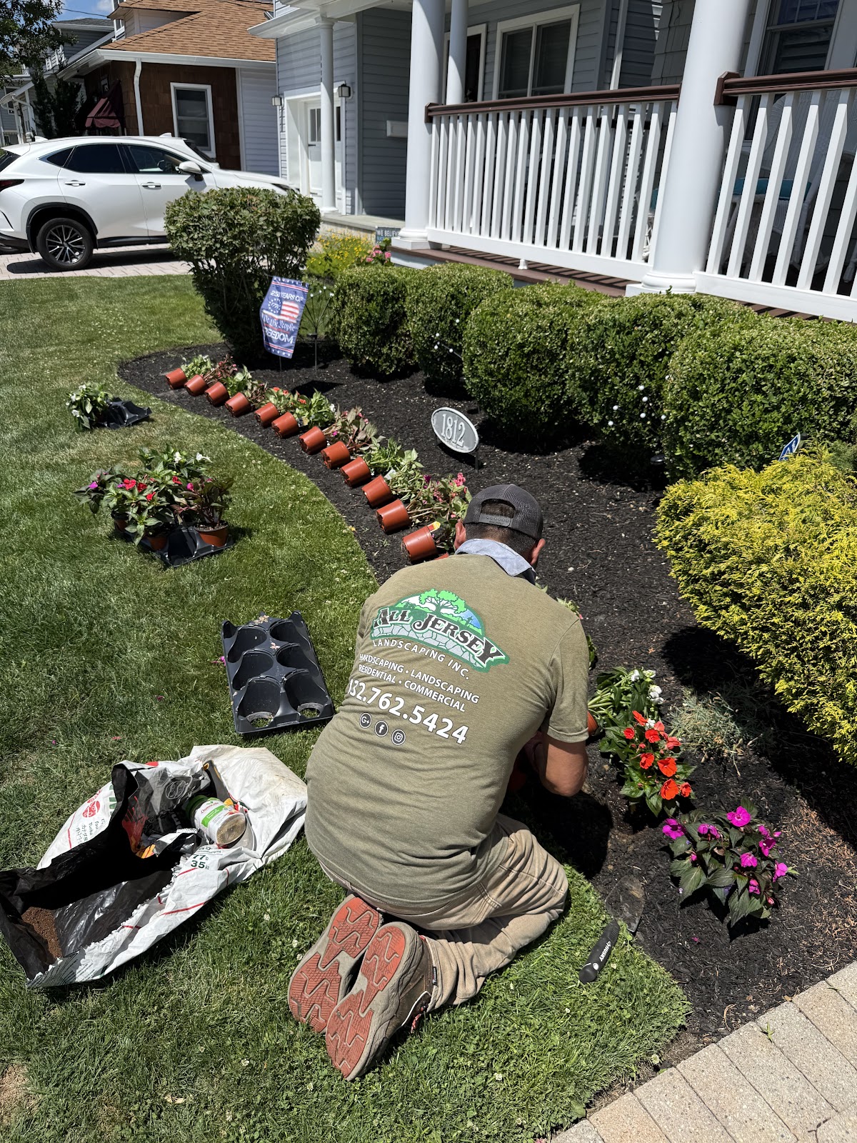 All Jersey Landscaping crew member in branded shirt planting flowers in a garden bed