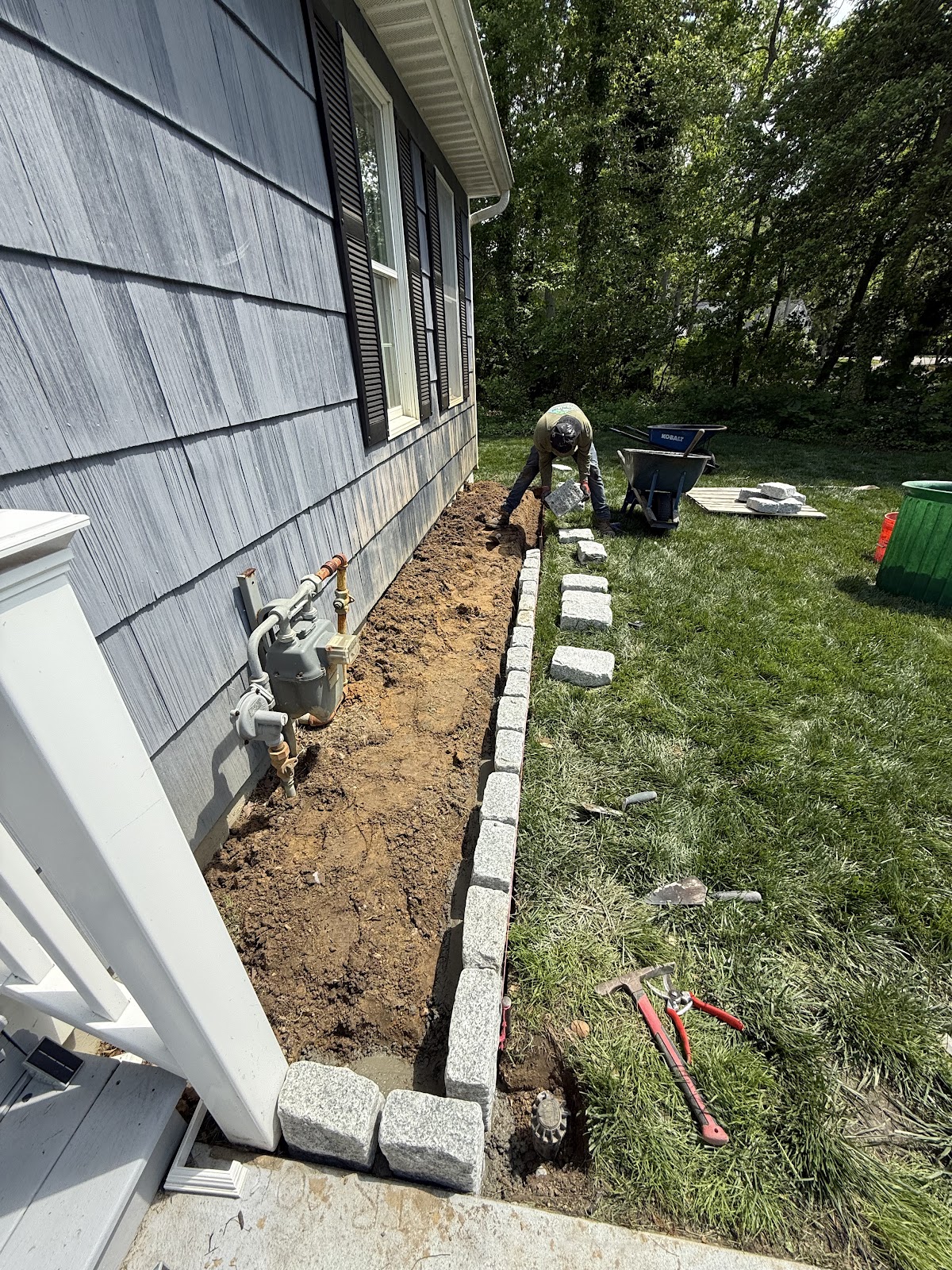 Crew installing granite Belgian block edging along a foundation